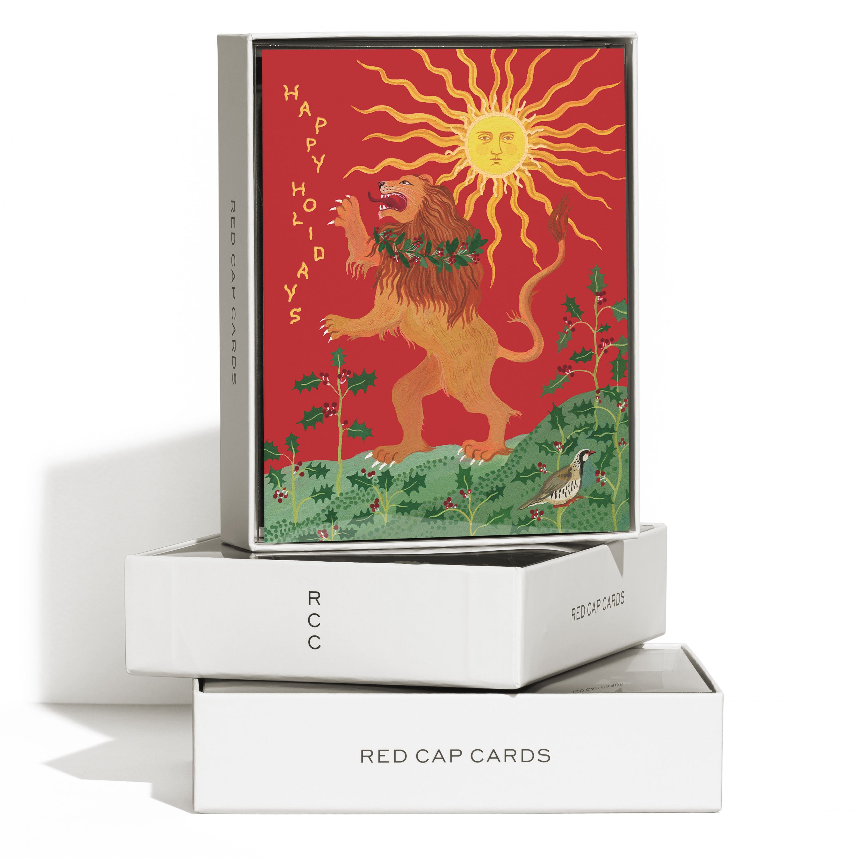 Boxed set of 'Happy Holidays' cards, roaring lion with holly wreath under sun with face, holly plants and bird on red background.