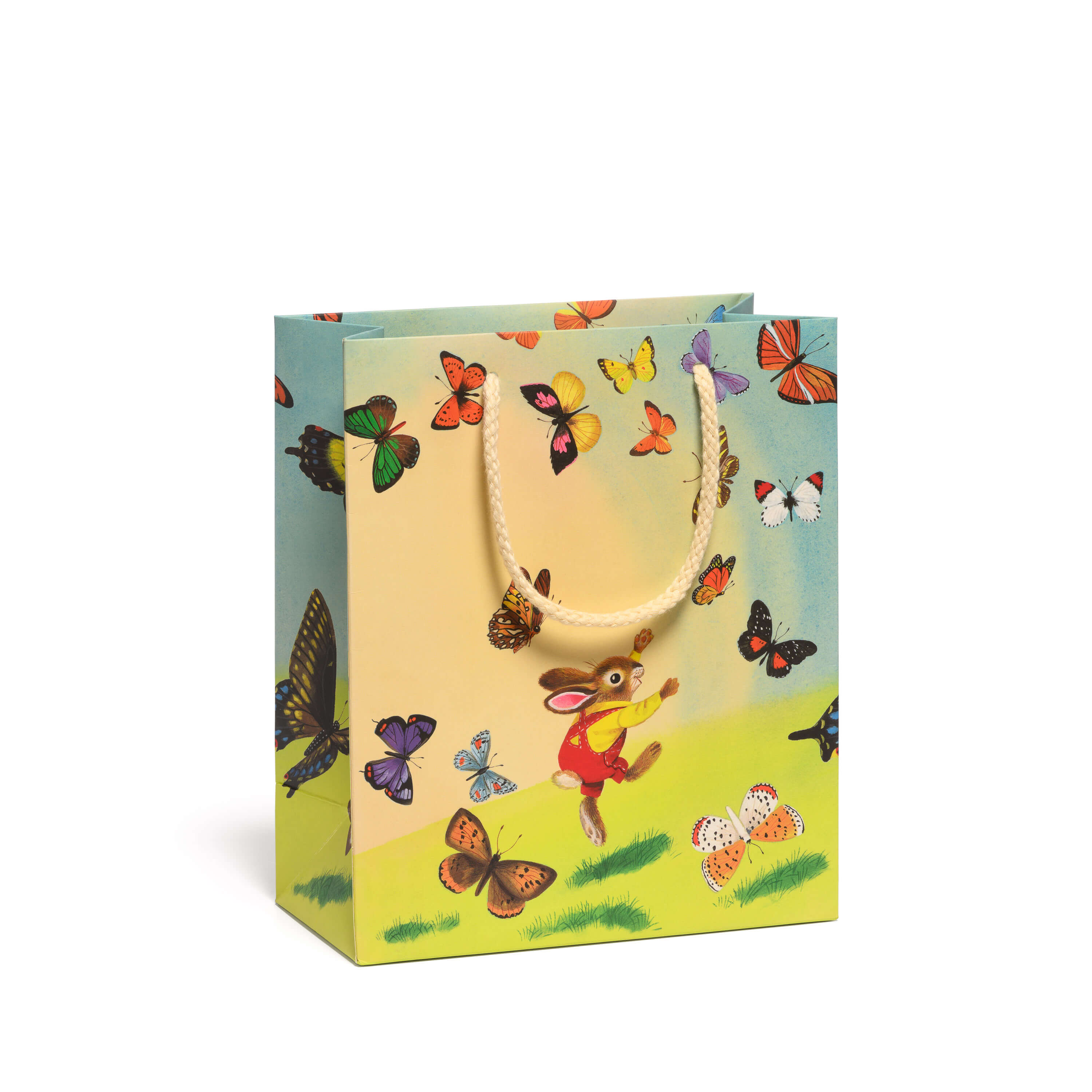 Gift bag with a cartoon bunny in red overalls chasing colorful butterflies in a grassy field on a white background.
