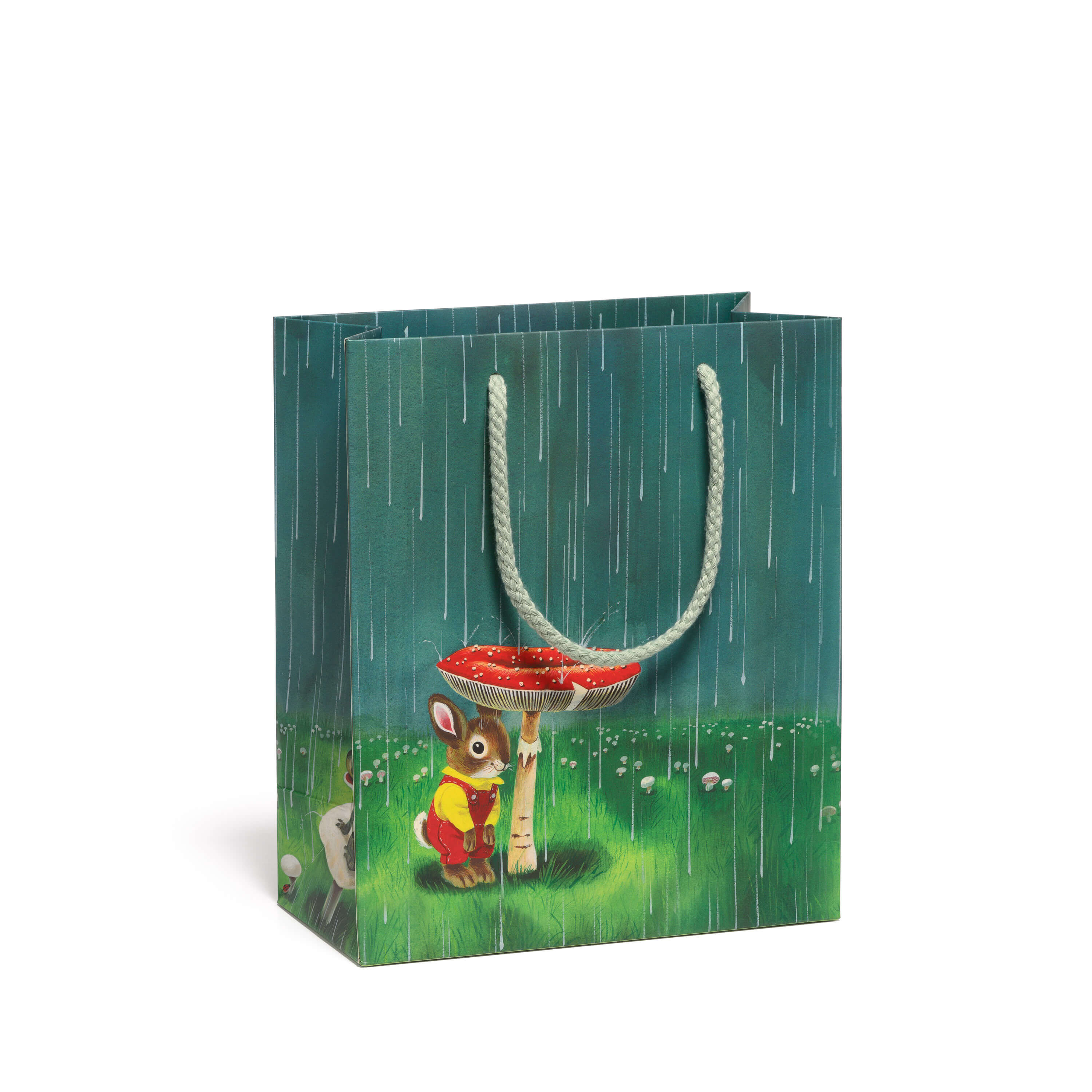 Gift bag with a cartoon bunny in overalls hiding under a mushroom in the rain in a green grassy field background.
