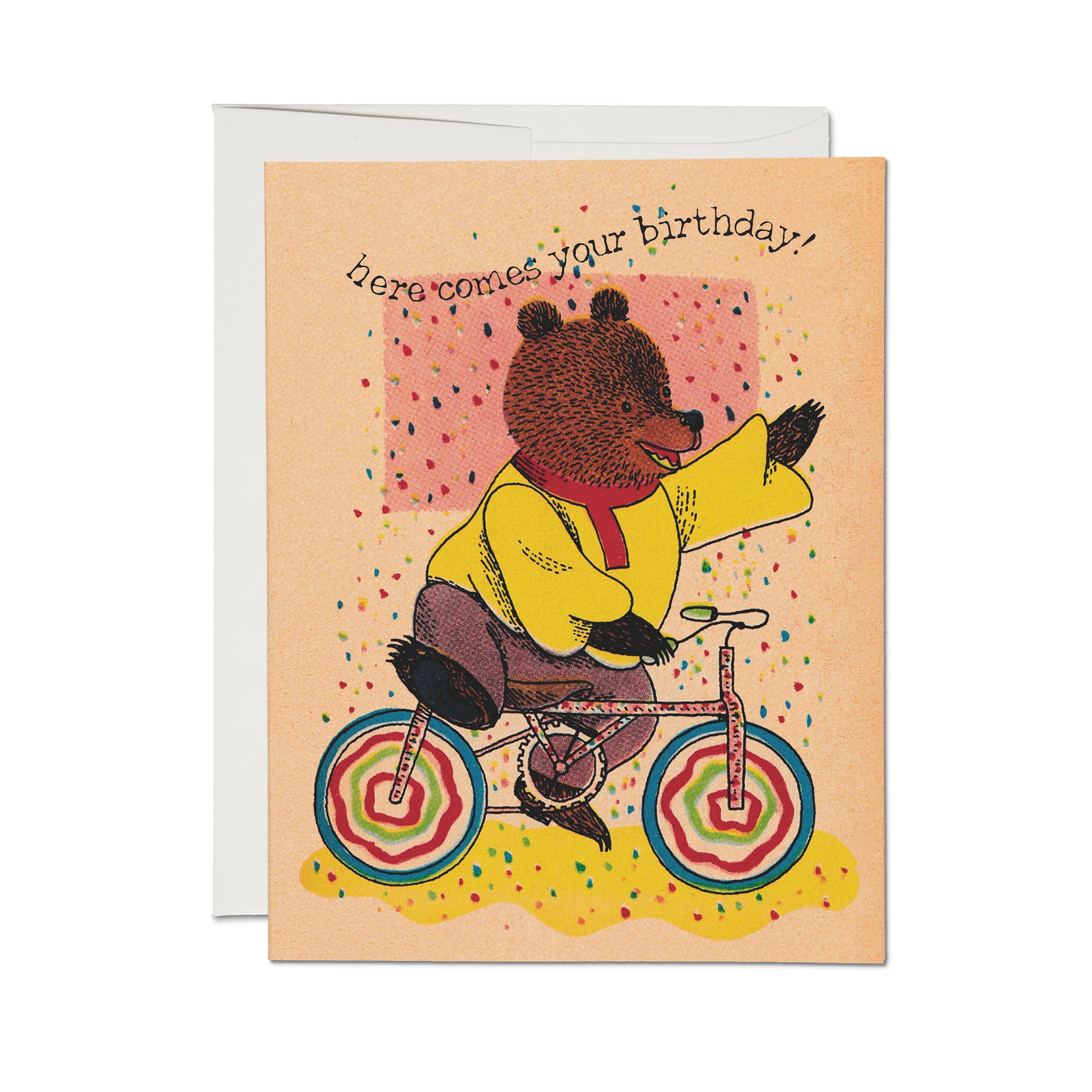 Birthday card with illustrated bear riding a bicycle and "here comes your birthday" text on peach background with confetti.