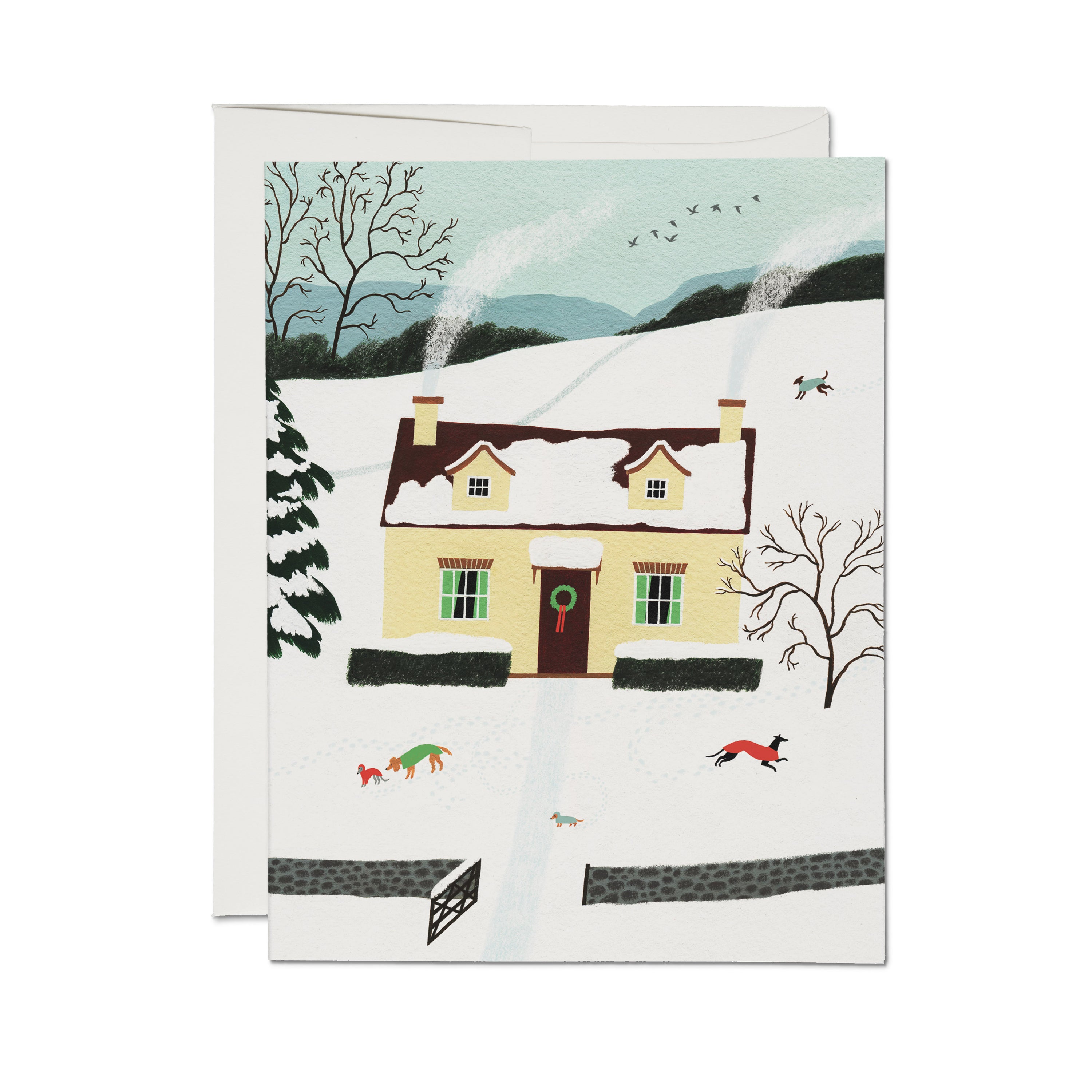 Christmas card with snowy yellow house, wreath on door, dogs in sweaters playing in snow, birds flying, winter landscape.