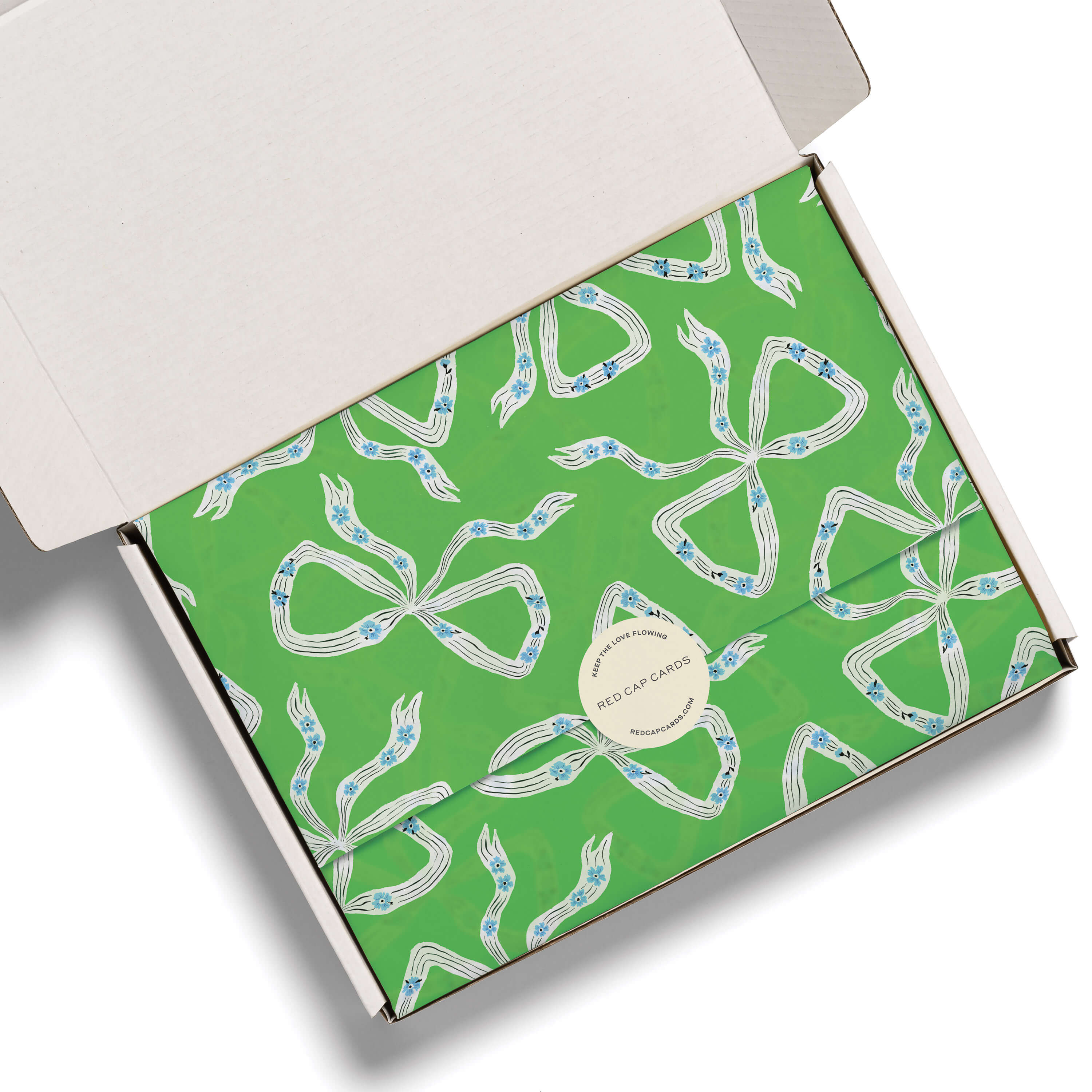 Green tissue paper with white and blue bow design in a white box on a white background.
