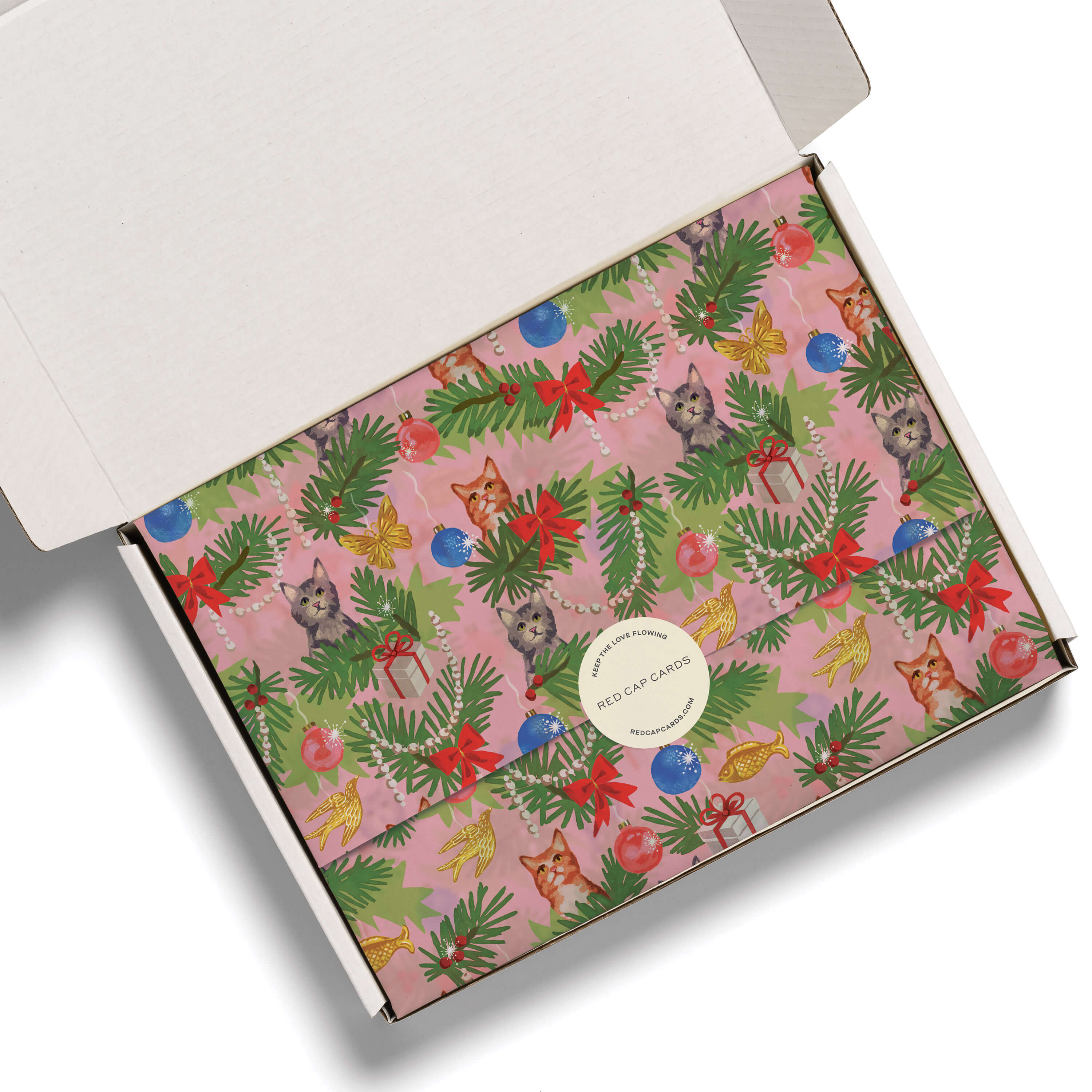 Tissue paper with an illustrated design of cats in a Christmas tree with ornaments, presents on pink background in white box.
