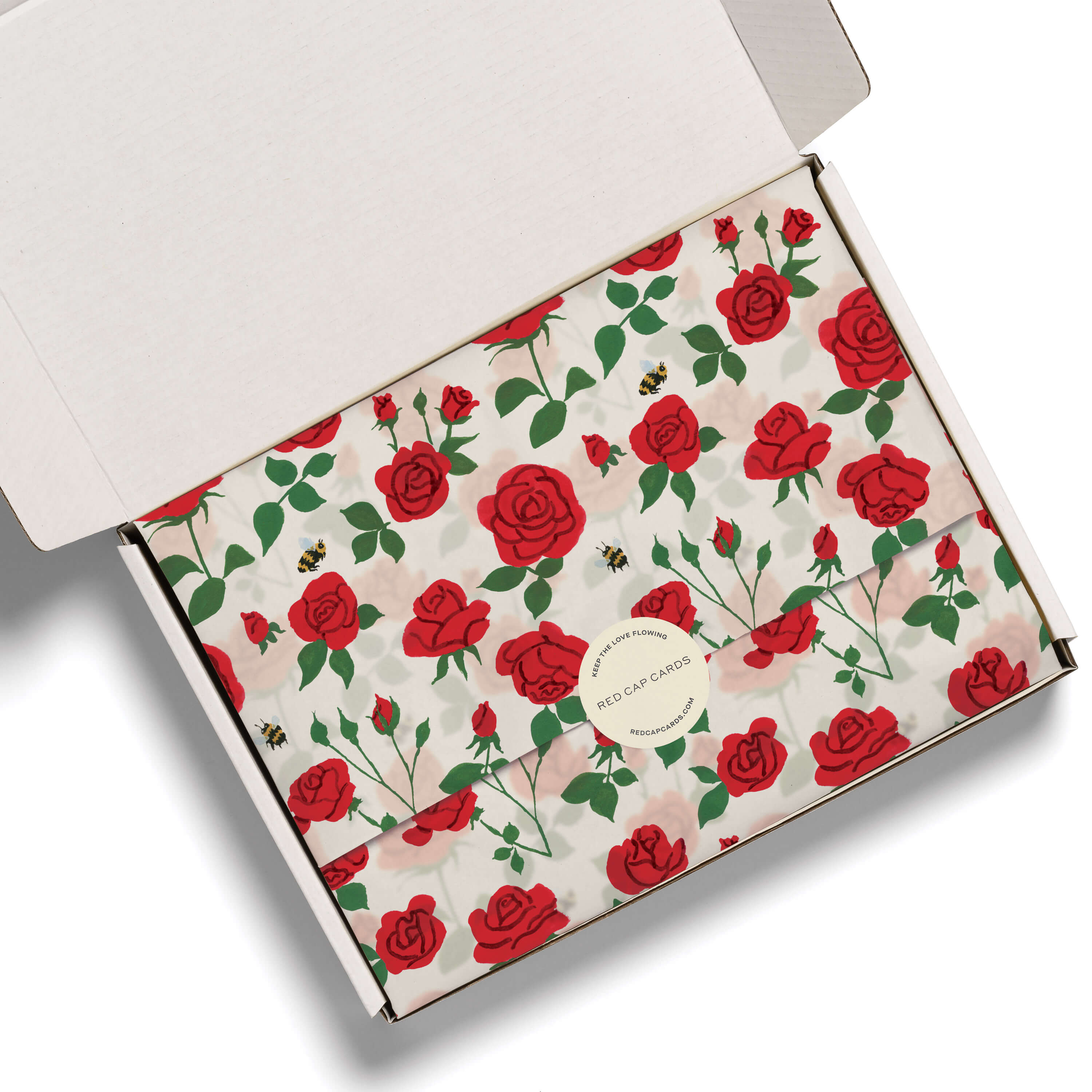 Tissue paper with illustrated blooming red rose and bee pattern in a white box on a white background.