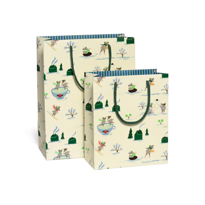 Two patterned paper bags with ice skating mice pattern with green handles on a white background.